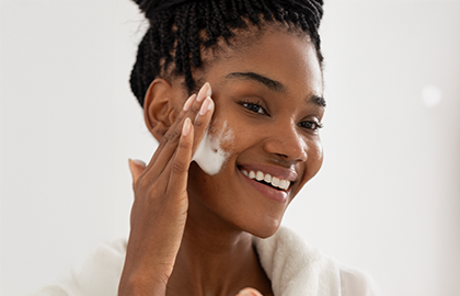 Uma mulher negra sorrindo passando light velvet no rosto demonstrando auto-cuidado com a pele.