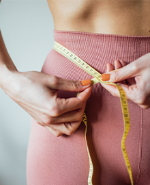 Mulher usando uma fita métrica para medir sua cintura, simbolizando cuidado com a saúde.