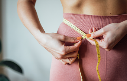 Mulher usando uma fita métrica para medir sua cintura, simbolizando cuidado com a saúde.