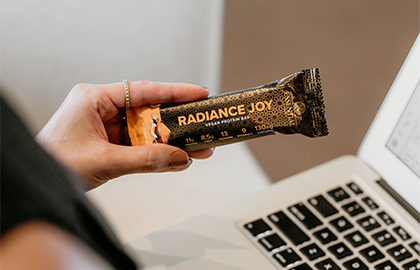 Mulher segurando a barra de proteína Radiance Joy Essential Nutrition, com foco na nutrição essencial e sabor.