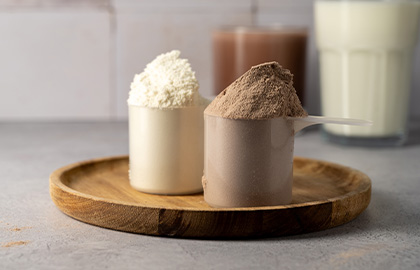 Dois scoops de proteína bovina em um prato de madeira, um de sabor cacau e outro de sabor banana com canela