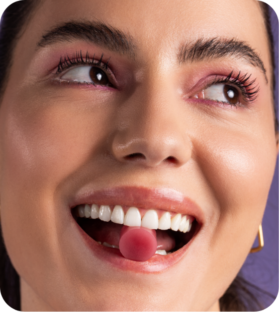 Mulher sorrido com uma creatina em goma sabor jabuticaba na boca.
