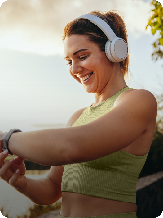 Mulher usando fone de ouvido e sorrindo ao olhar para o seu smartwatch após corrida.