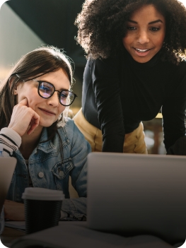 Duas mulheres observando atentamente um laptop, compartilhando ideias e interagindo com a tela.