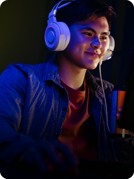 Homem usando fones de ouvido e headset, concentrado em frente a um computador, em ambiente de trabalho.