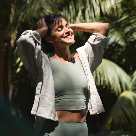 mulher sorrindo ao ar livre com roupa de academia verde, comemorando o funcionamento do seu sistema imunológico.