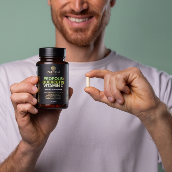 homem sorrindo, segurando um pote de própolis verde com vitamina c em uma das mãos e uma cápsula de própolis verde na outra mão